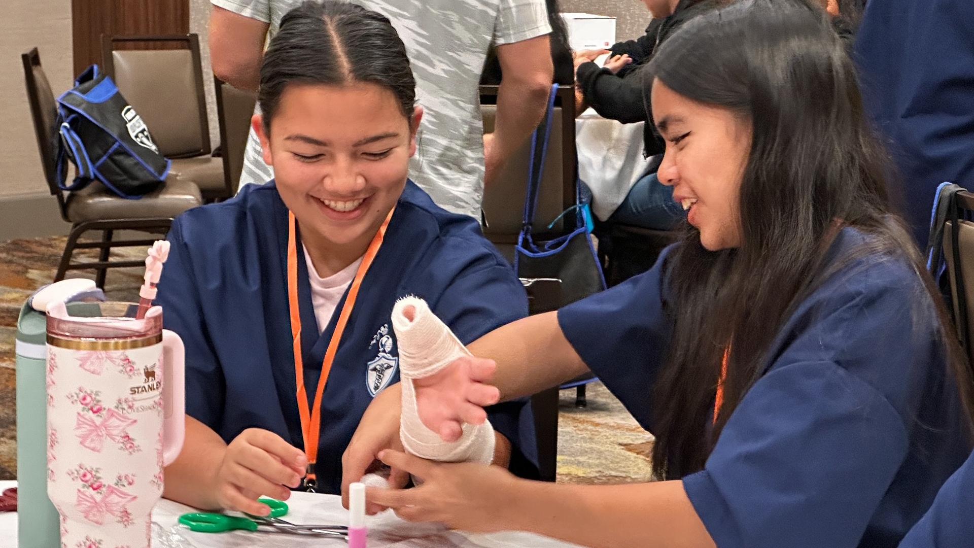 Two smiling students practice splinting while sitting at a table together.