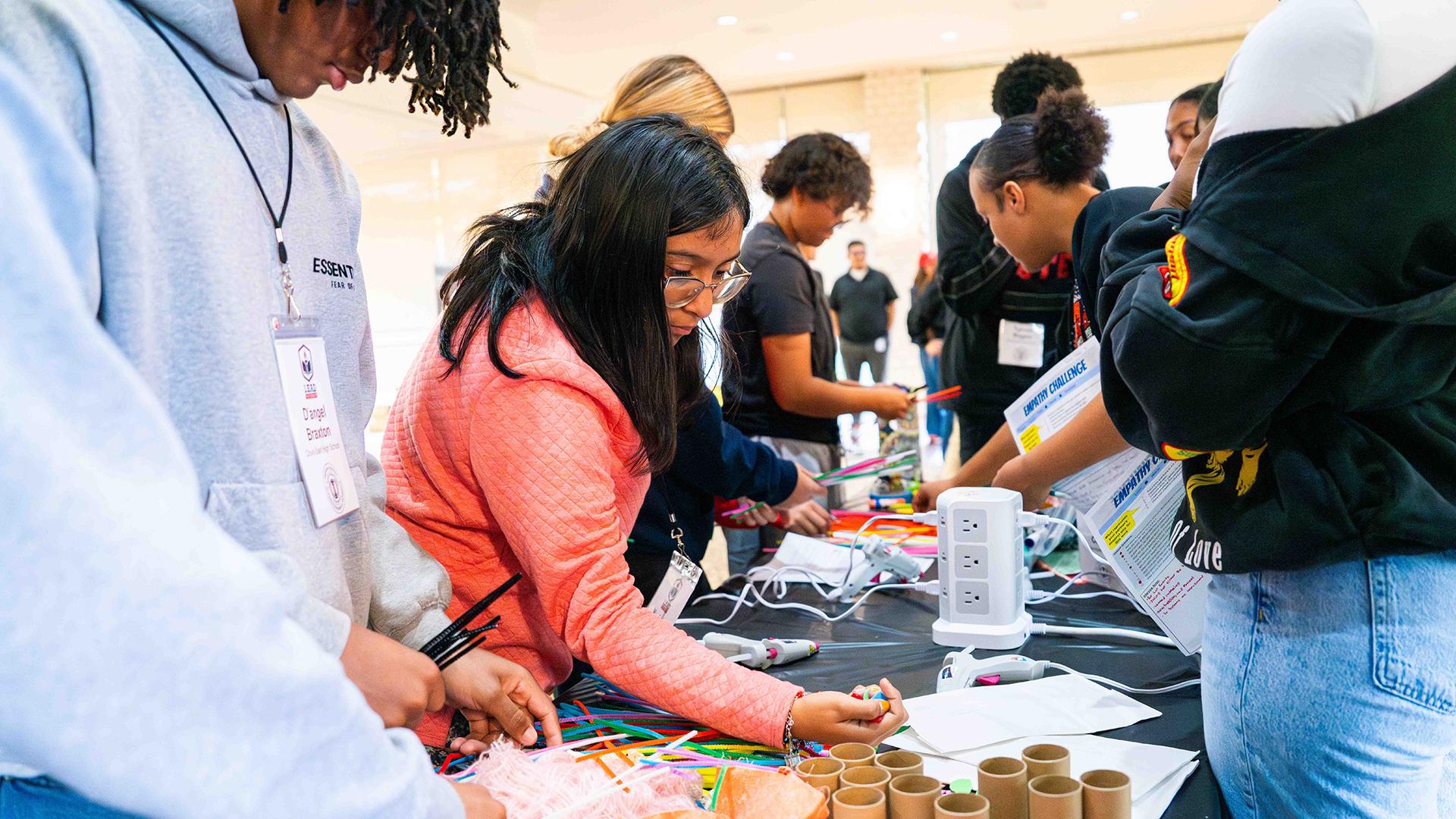 Students are choosing art supplies from a table to participate in a creative exercise.