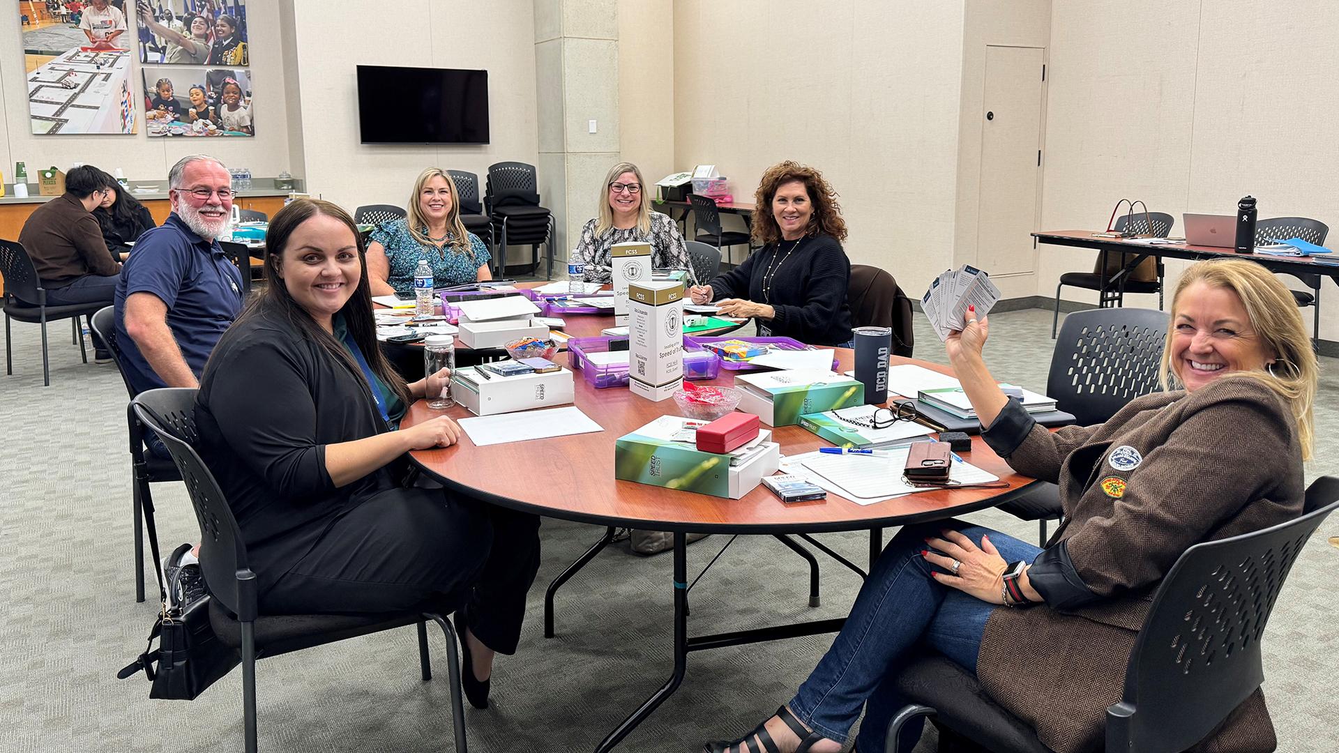 Smiling participants are sitting at a table with their meeting materials in front of them.