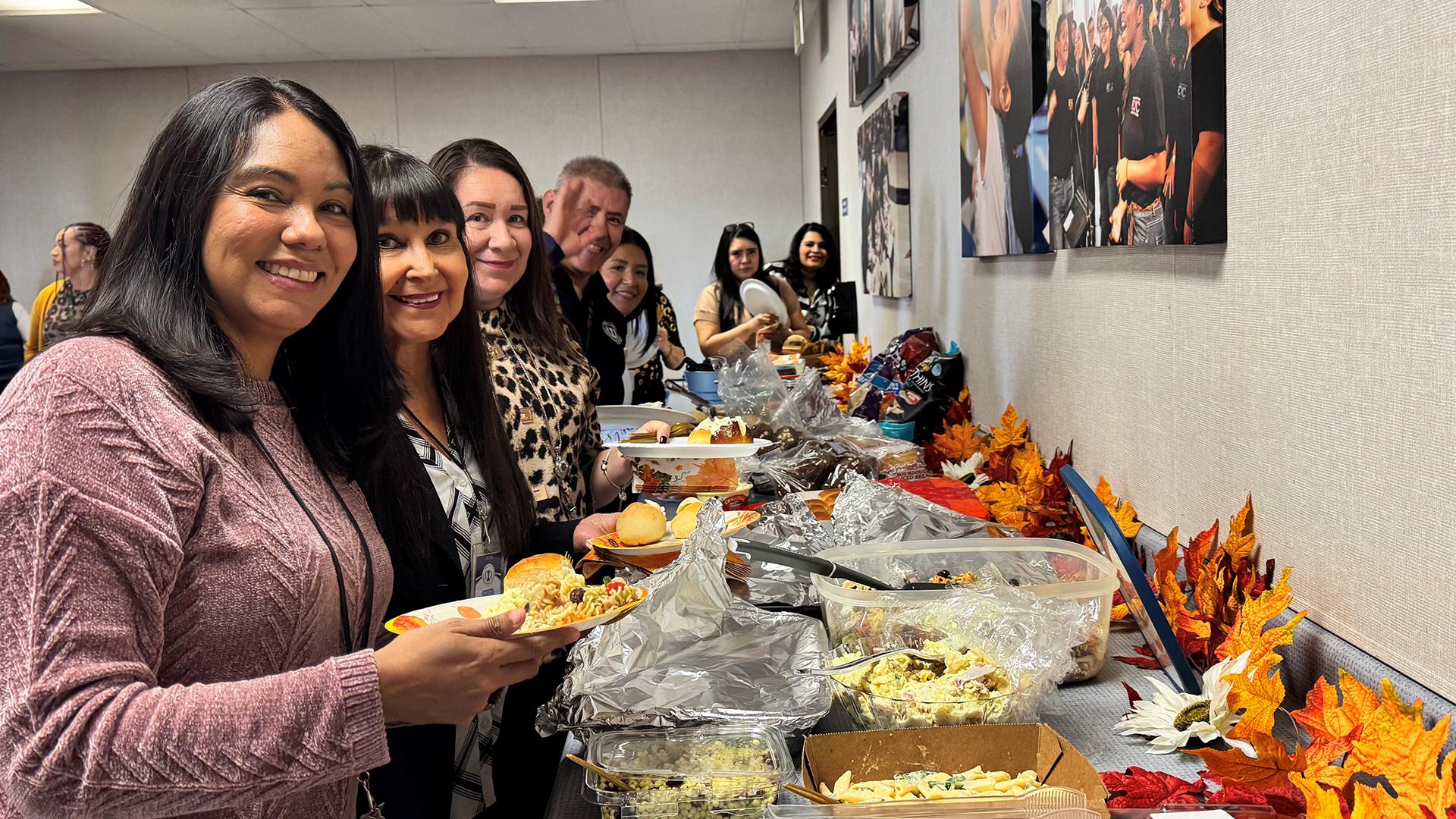 Smiling people holding plates are going through the potluck line choosing food.