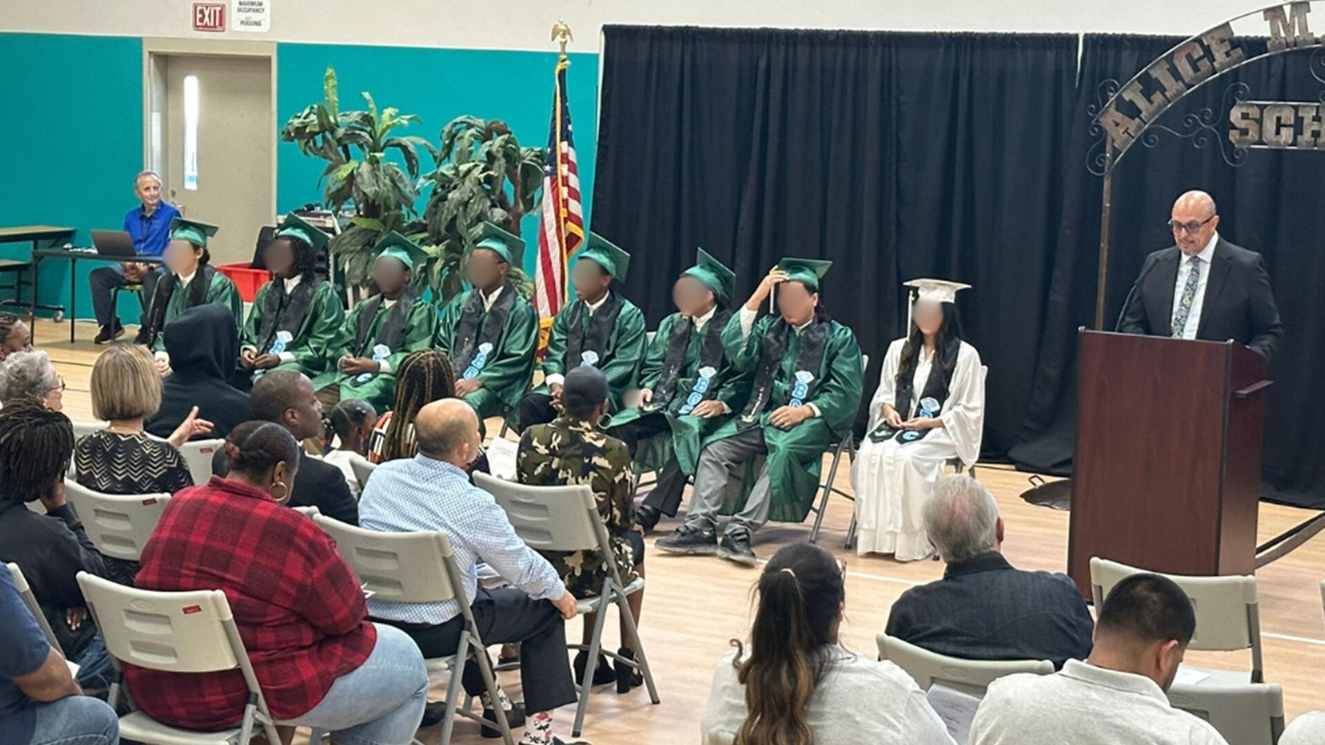 Graduates are sitting on chairs facing the guests while a speaker addresses the crowd.