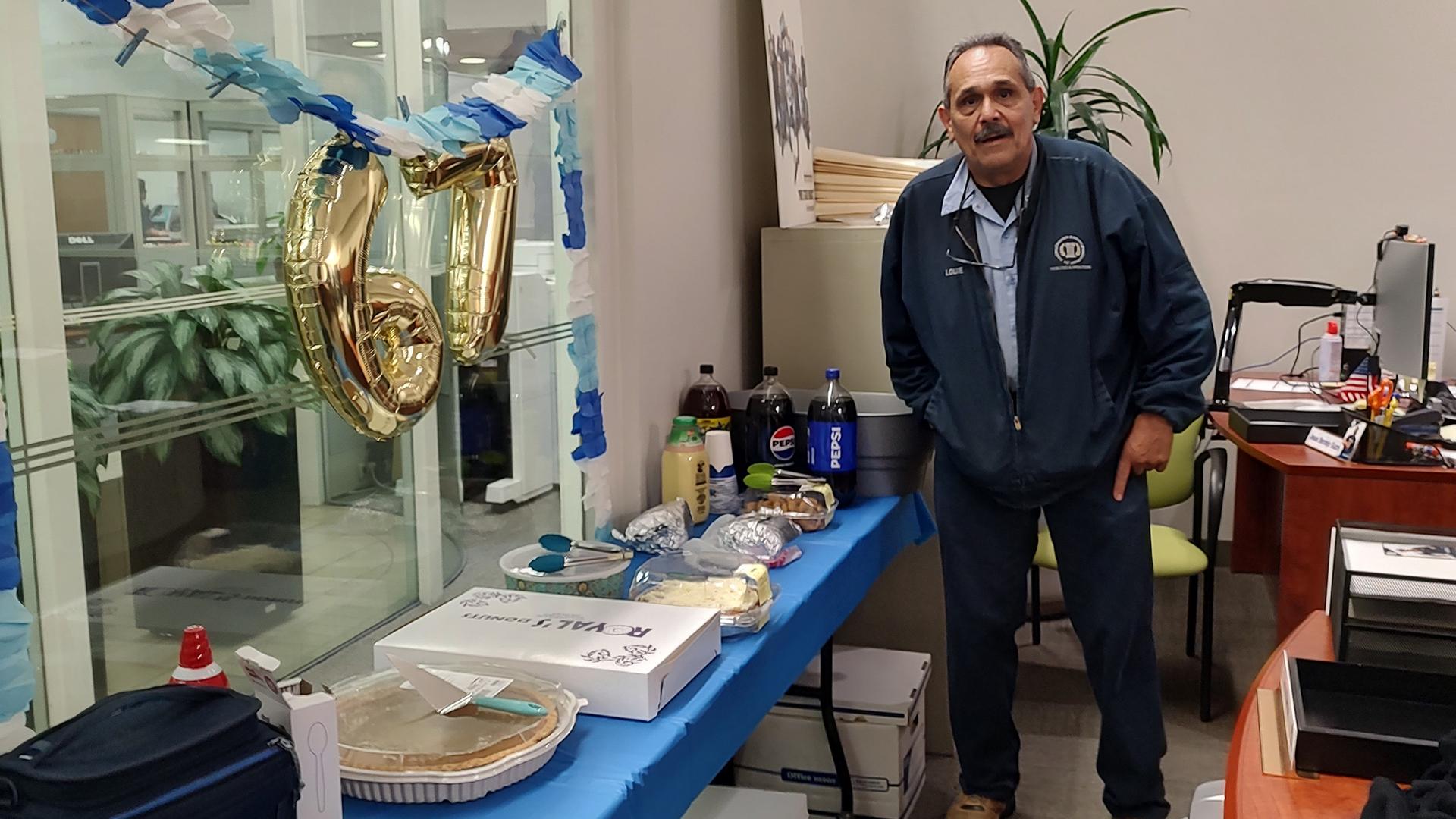 The person being honored is standing at a table with cake, treats and beverages.