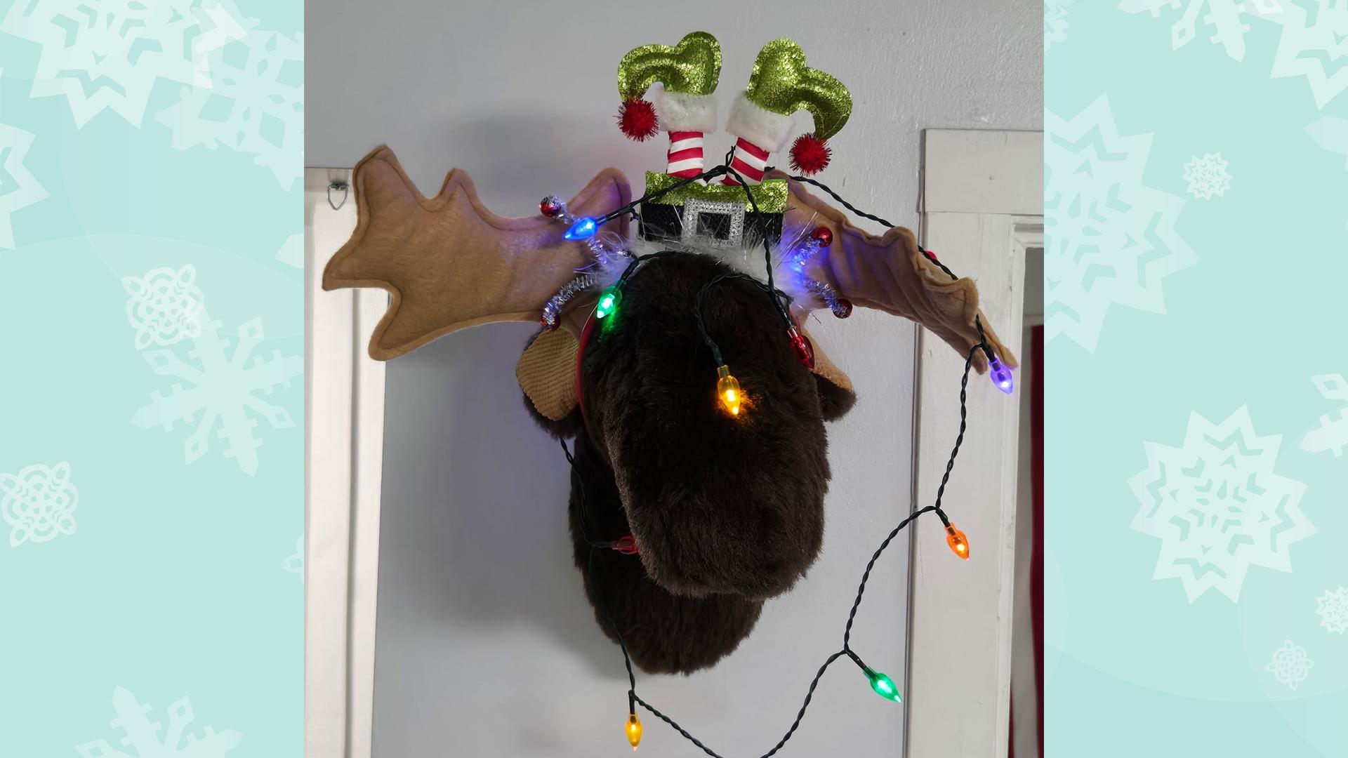 A plush moose head is on the wall, festooned with holiday decorations.