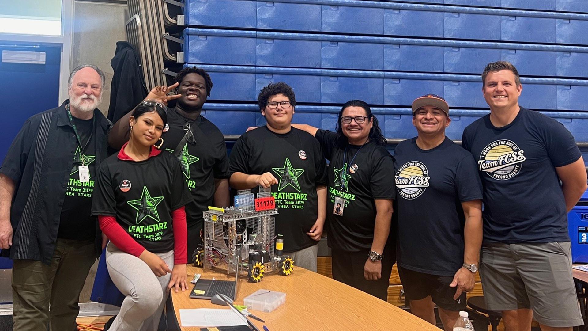 Happy students and staff are standing around a table with their robot displayed on the table.