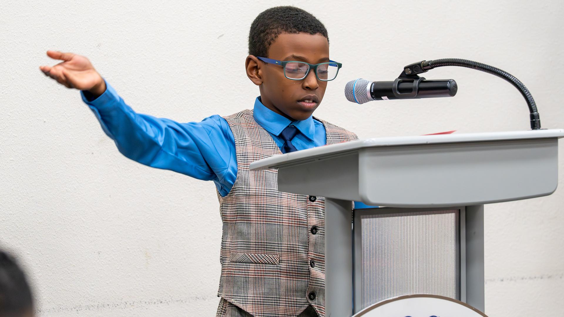 A boy is standing at a podium delivering his MLK speech.
