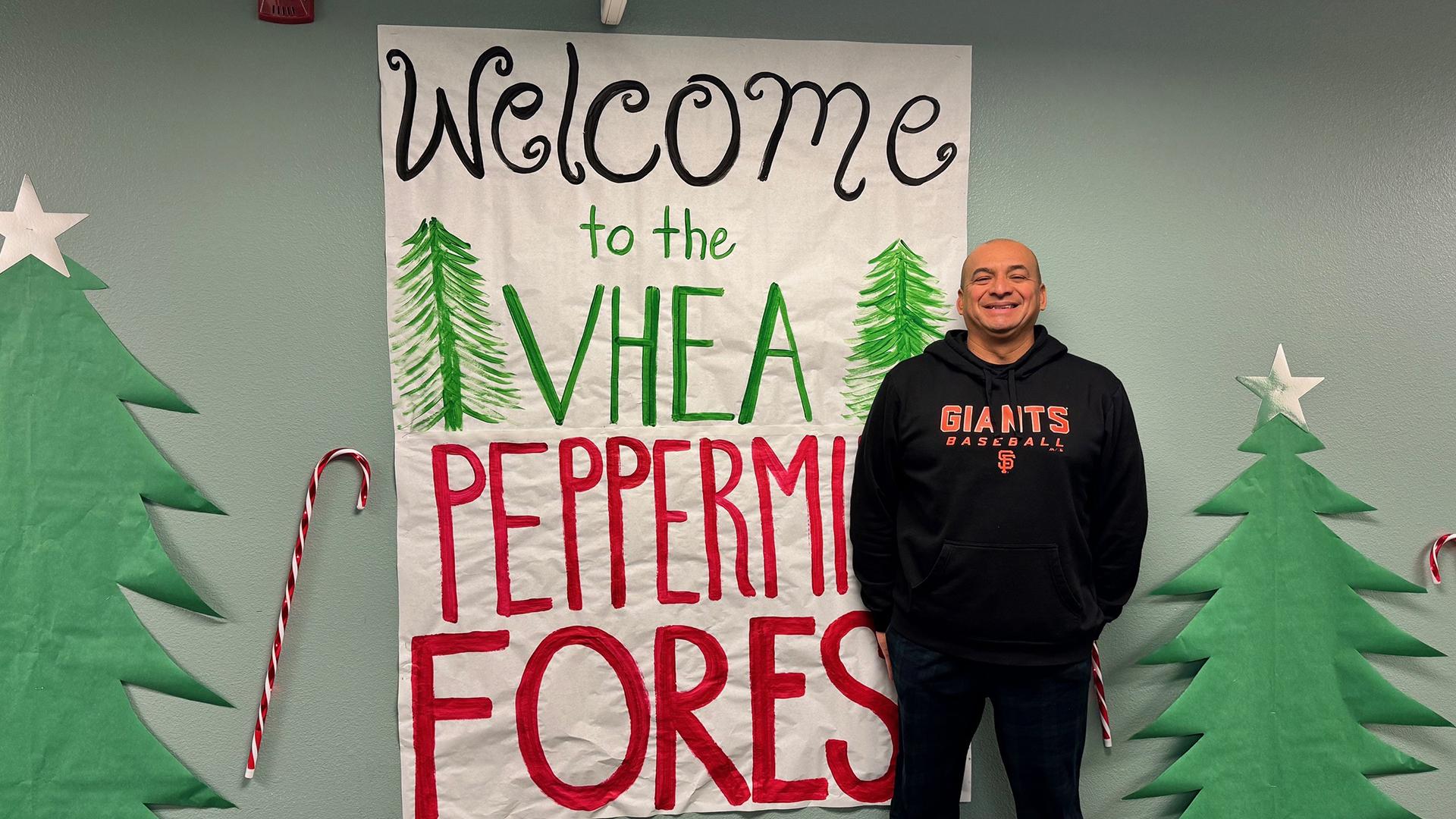 The Principal stands in front of a hall wall decorated with Christmas trees and candy canes.