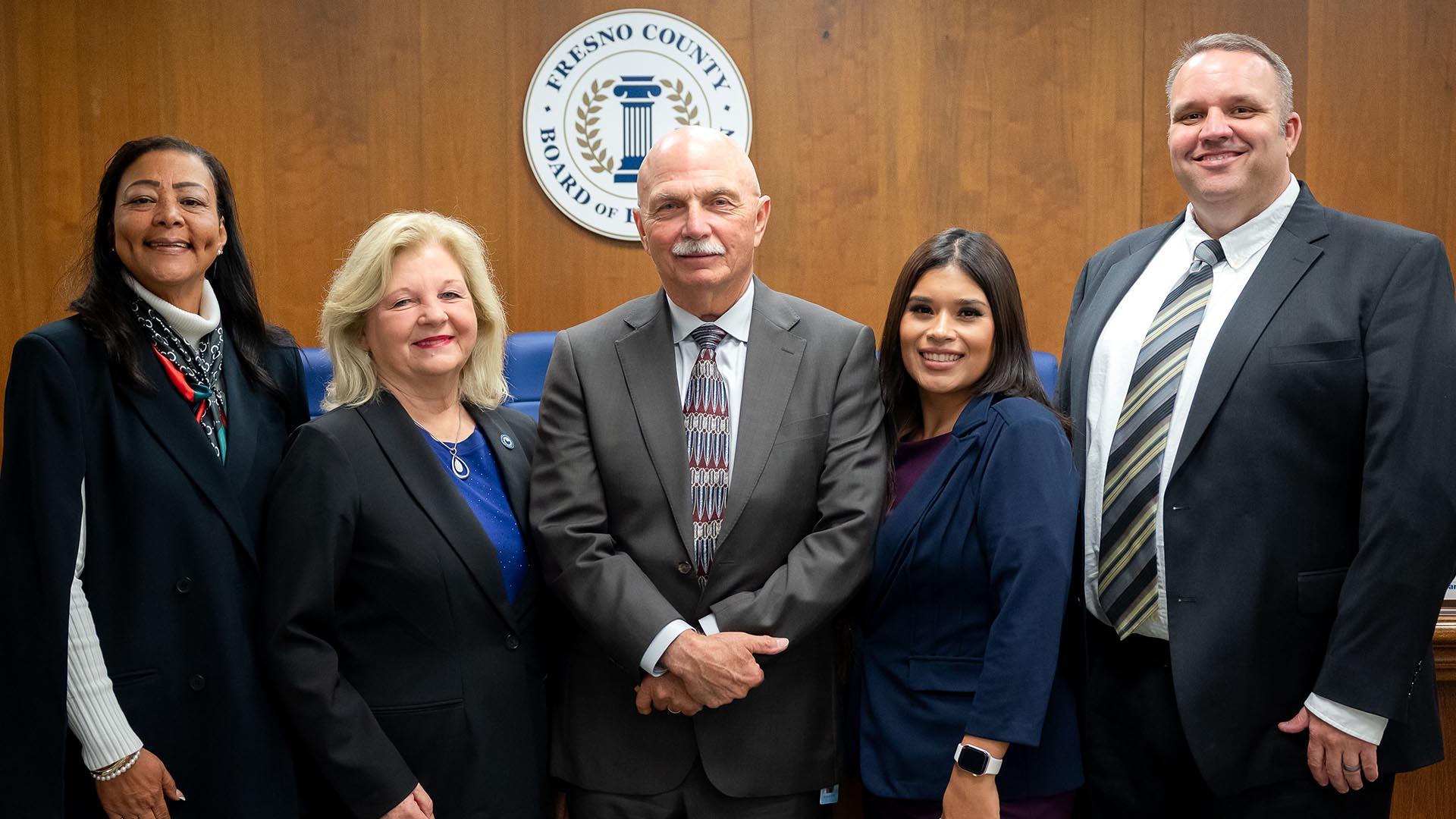 Five Fresno County Board of Education trustees stand in a line, smiling and facing forward.