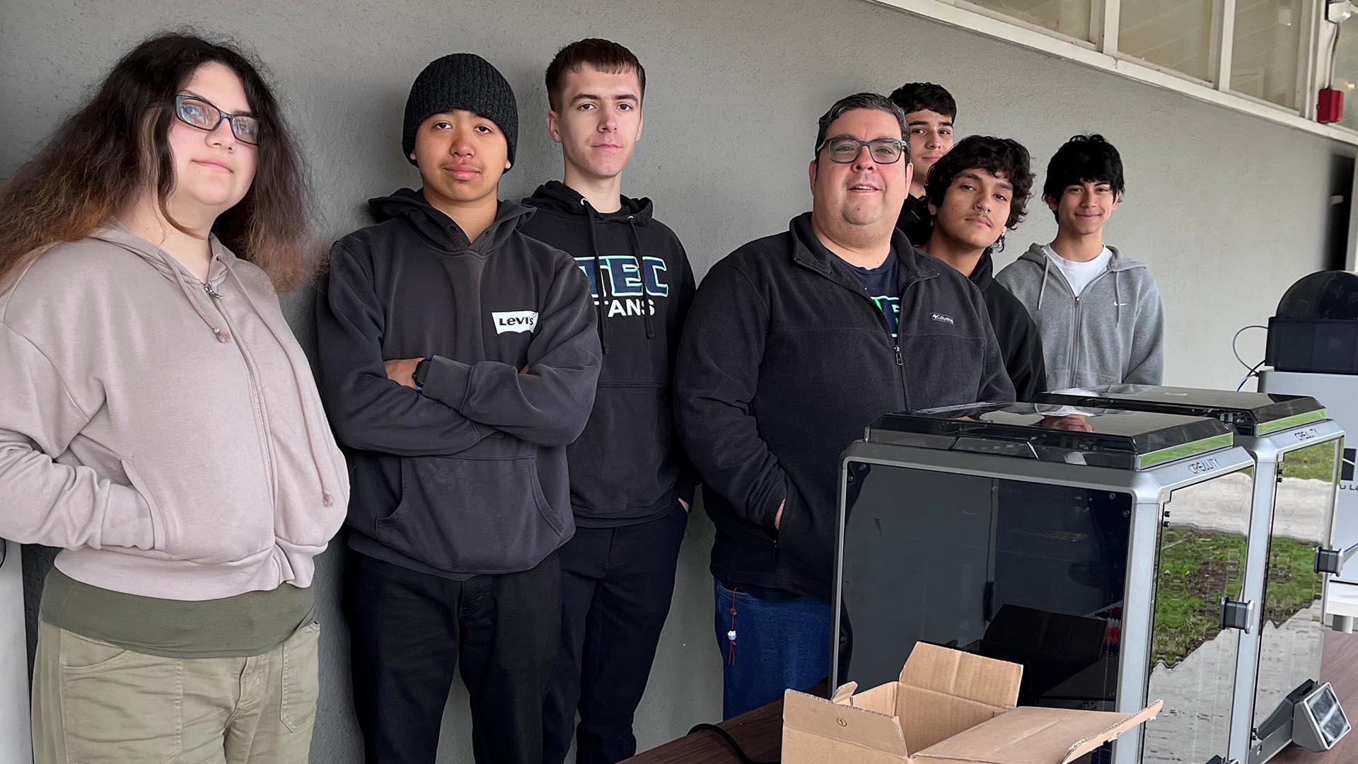 Students and staff stand behind a table that showcases the laser printer and name tags.