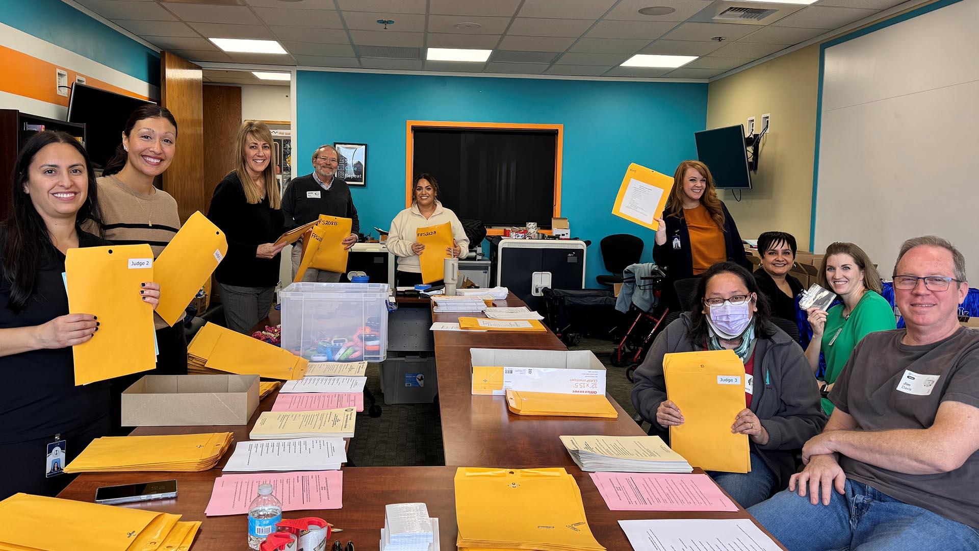 A group of smiling volunteers in a room stuffing packets for the event.