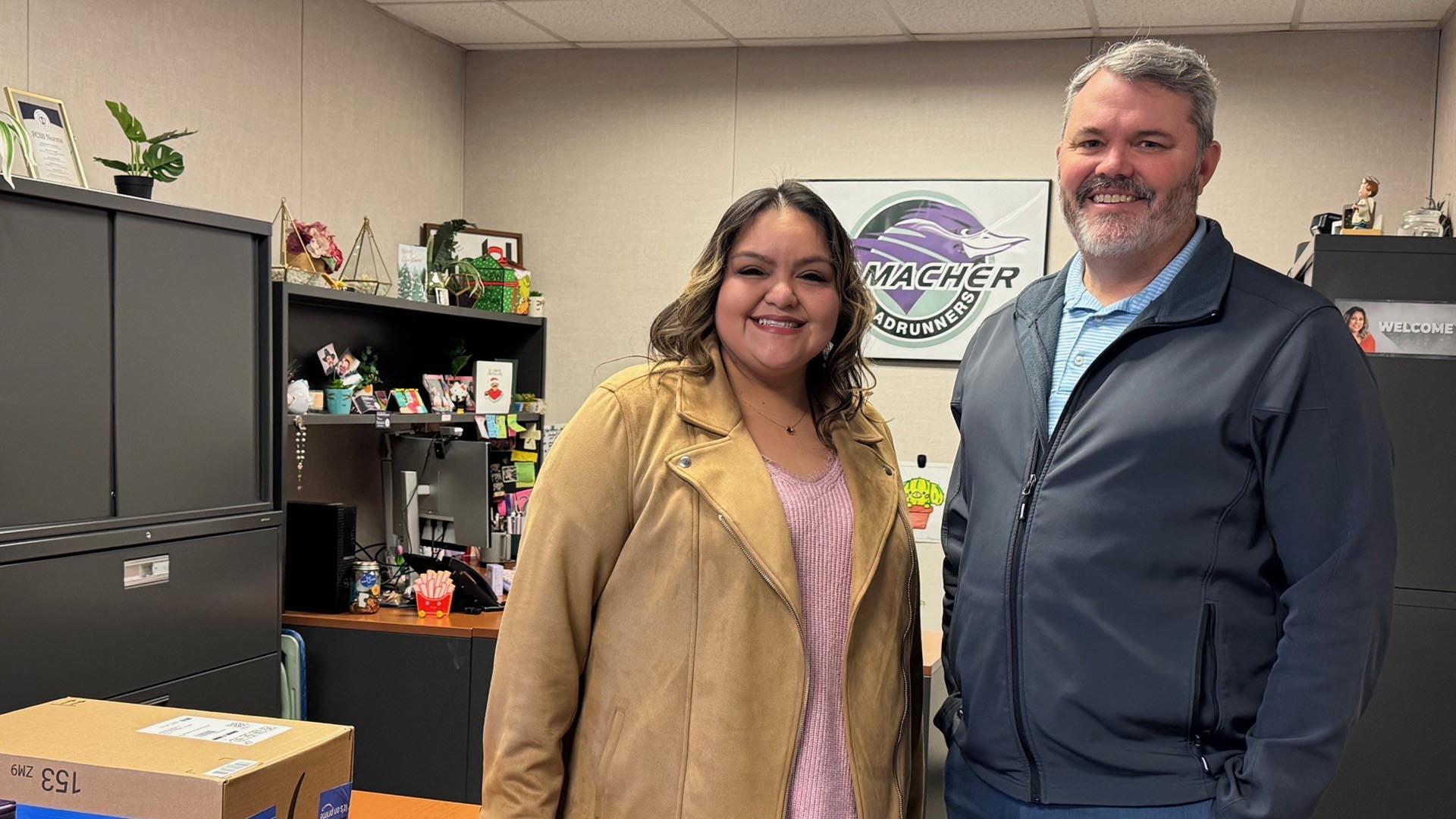 Two people are standing in the school's office, smiling.