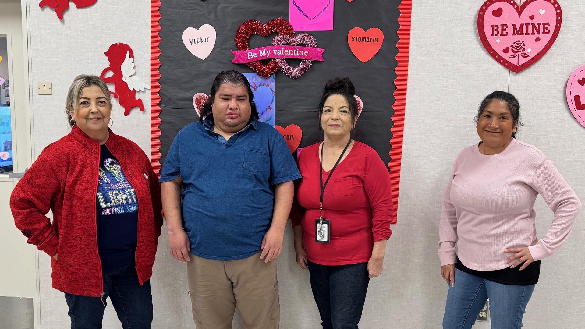 Four staff members are lined up in front of Valentine's decorations, smiling.