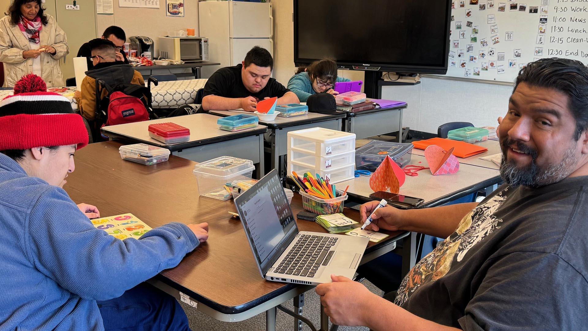 Students and staff are working together on lessons at tables.