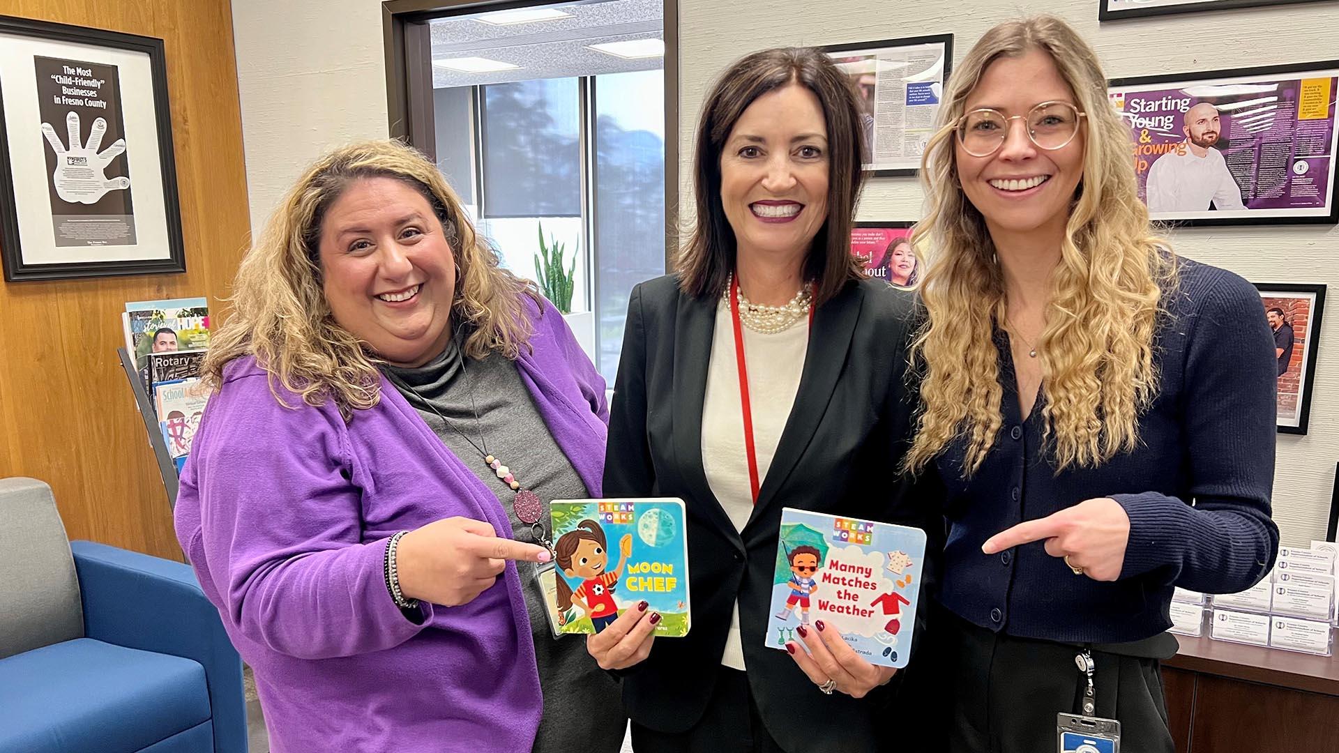 Three people stand together, holding two new books to be published.