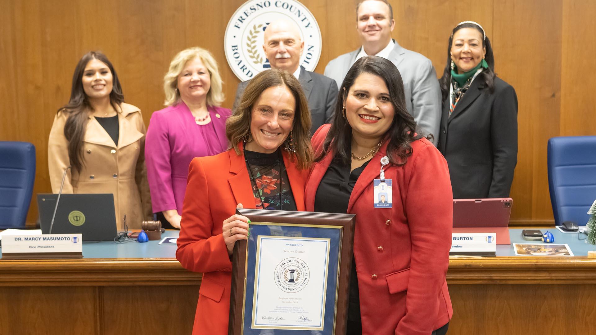The honoree stands with the Deputy Superintendent and the Fresno County Board of Education, holding her plaque.