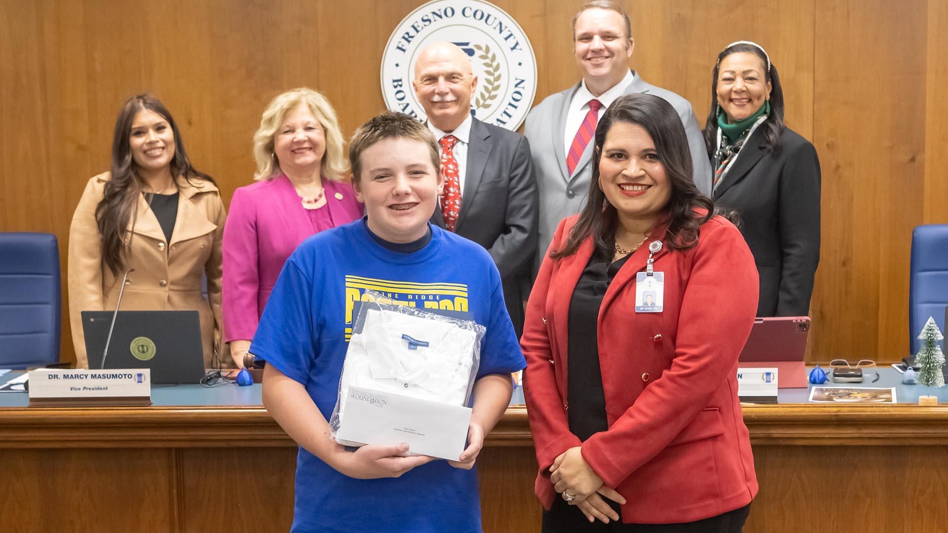 The honoree stands with the Deputy Superintendent and the Fresno County Board of Education, holding his plaque.