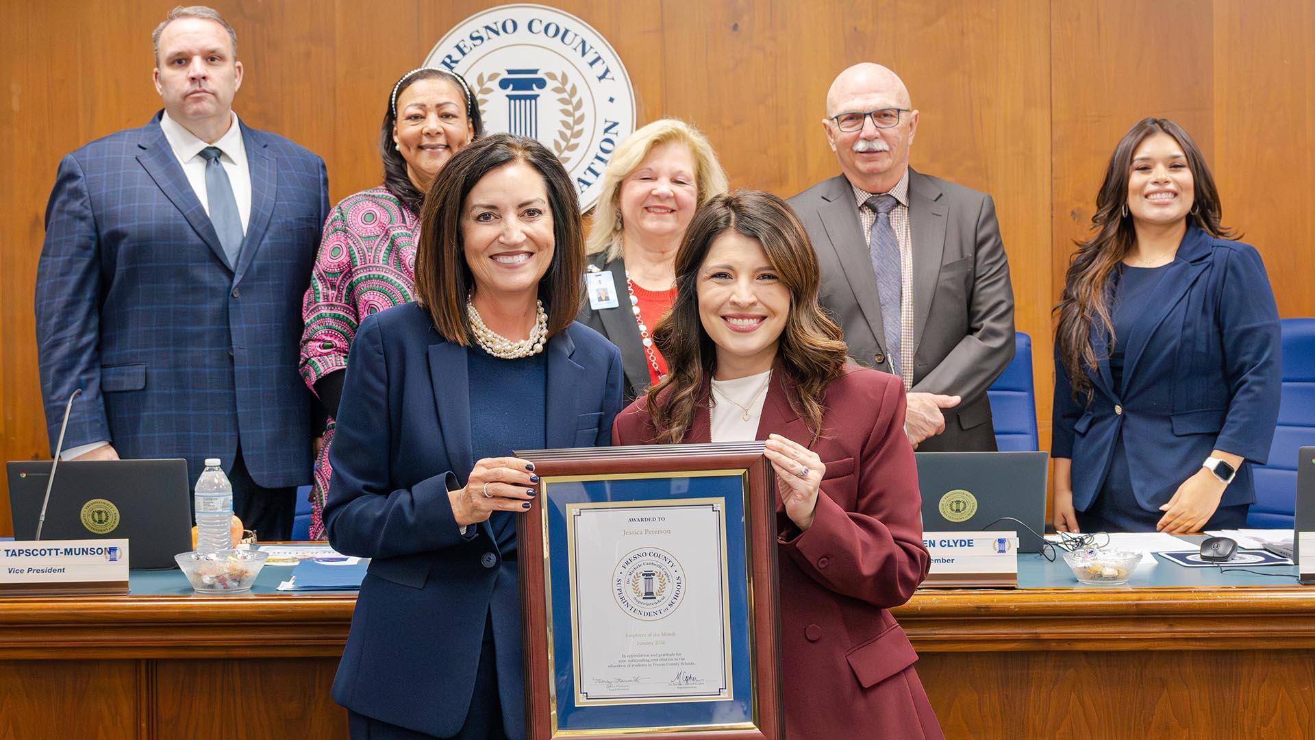 The honoree stands with the Superintendent and the Fresno County Board of Education, holding her plaque.