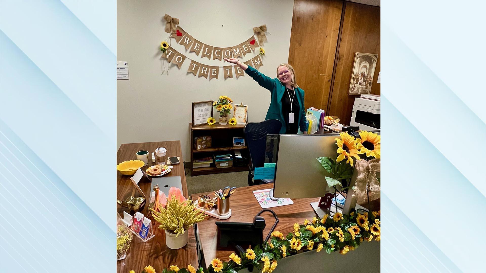 The honoree is standing and smiling, pointing toward her welcome banner.