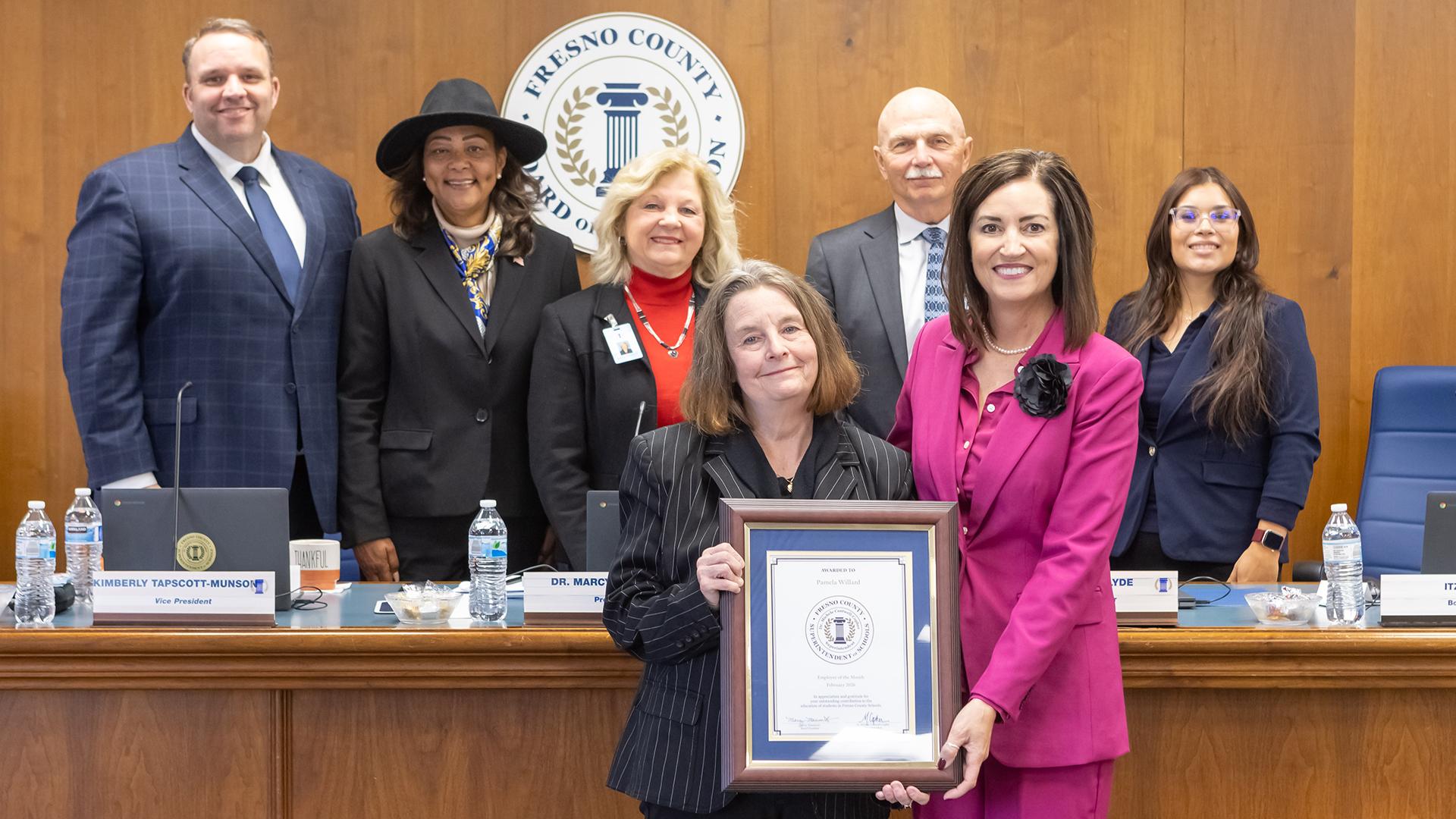A group of people are standing with the honoree, who is holding a plaque. 