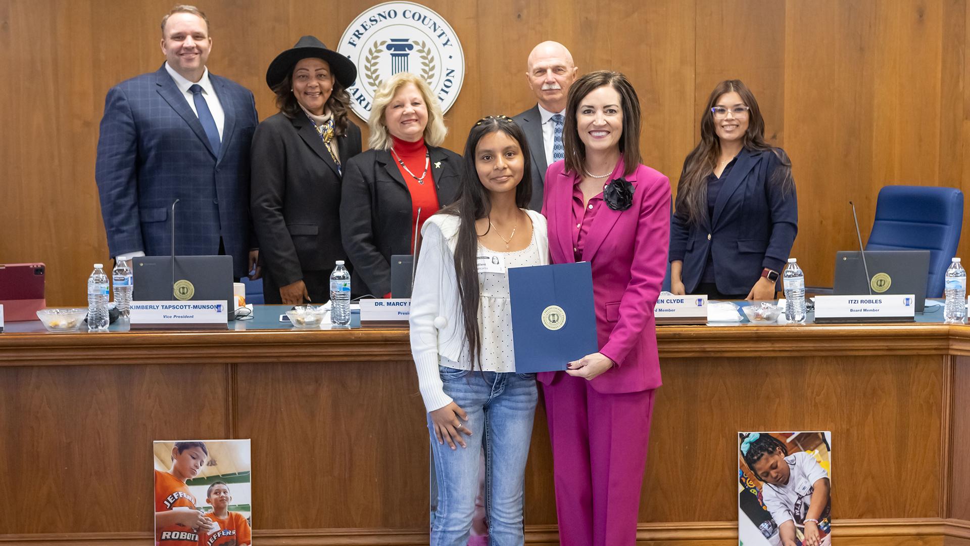A group of people is standing with the honoree, who is holding a certificate. 