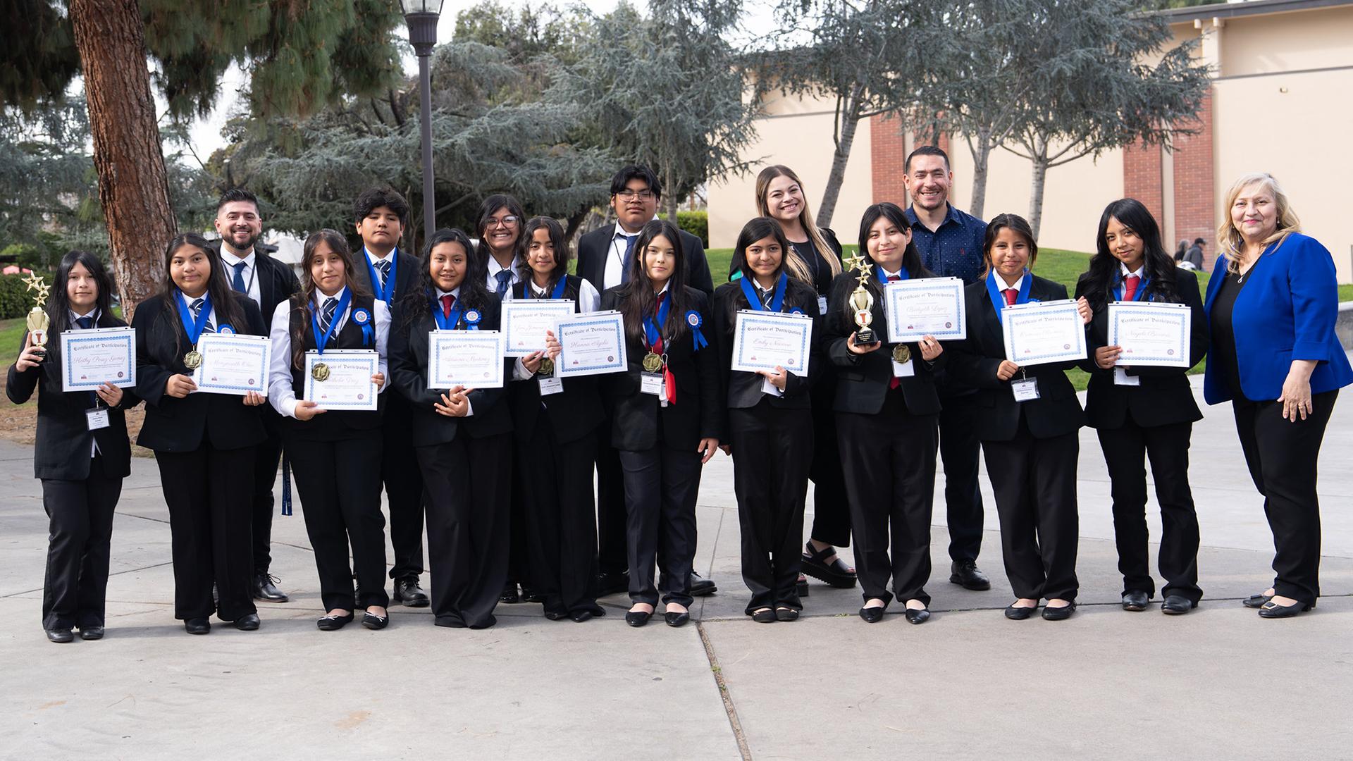 Students stand in a line, holding their certificates. 