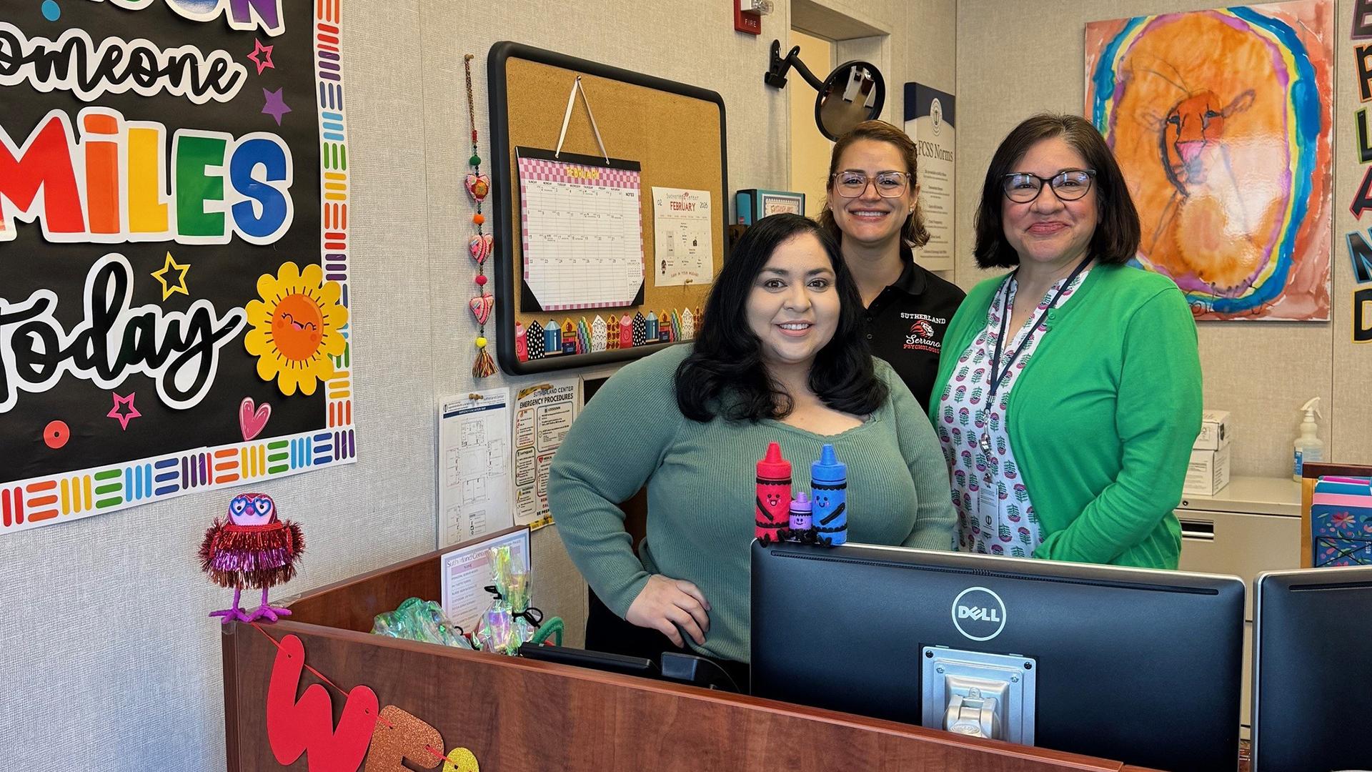 Three people stand together in the school office. 