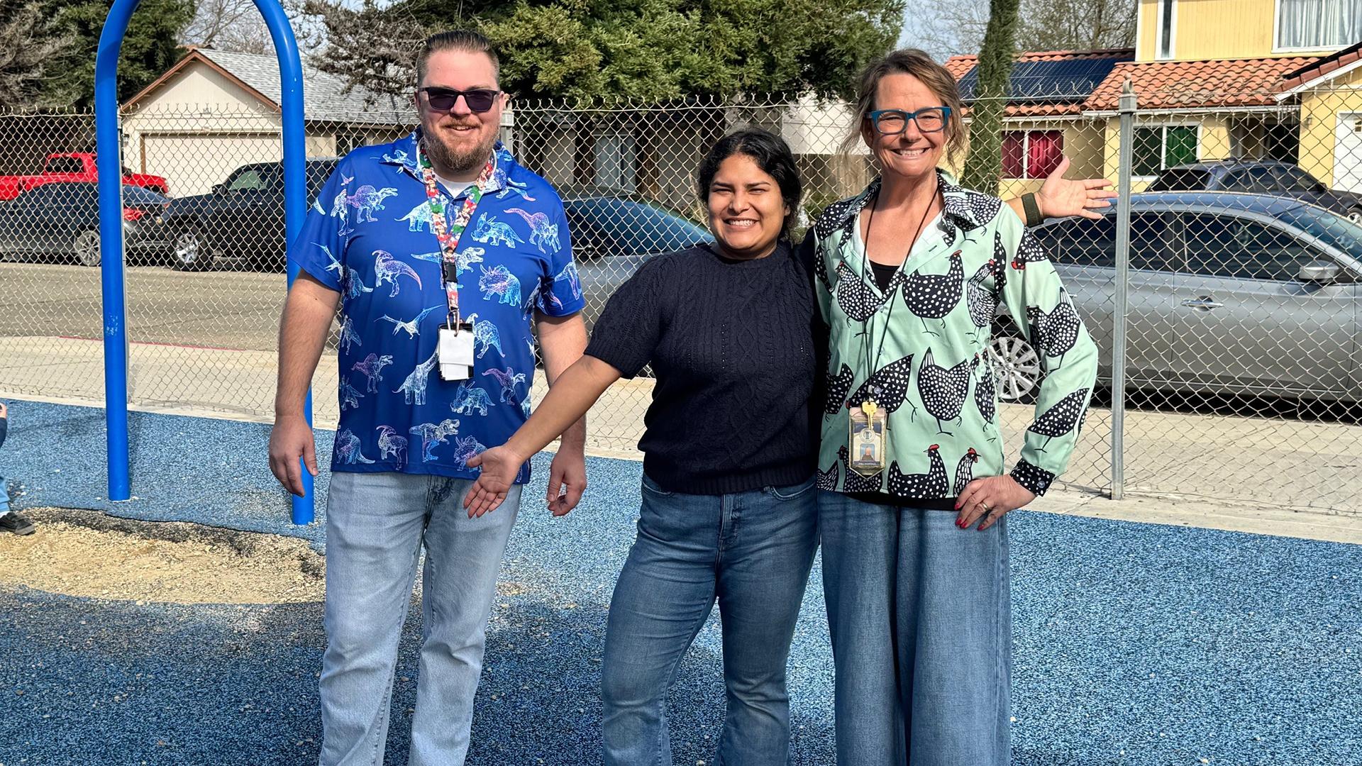 Three staff members stand together on the playground. 