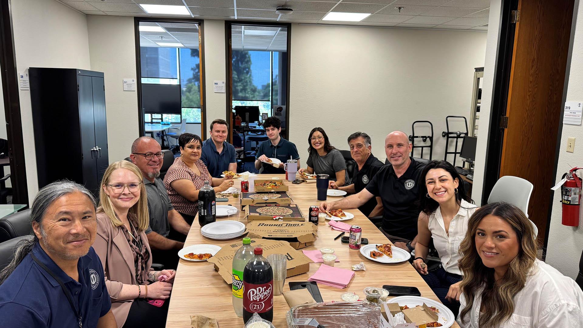 People sit at a table, eating pizza. 