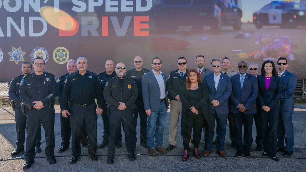 A group of law enforcement and other community partners are standing in front of a campaign billboard.