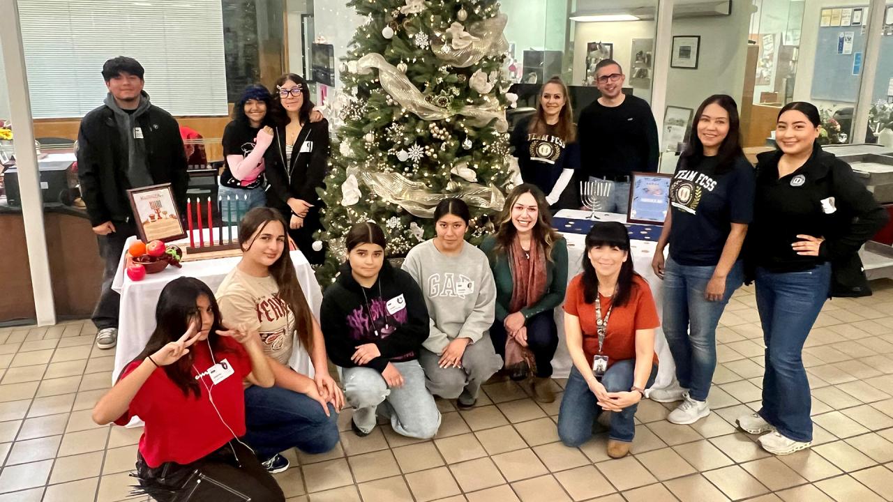 Students and staff are posed in front of a giant decorated Christmas tree.