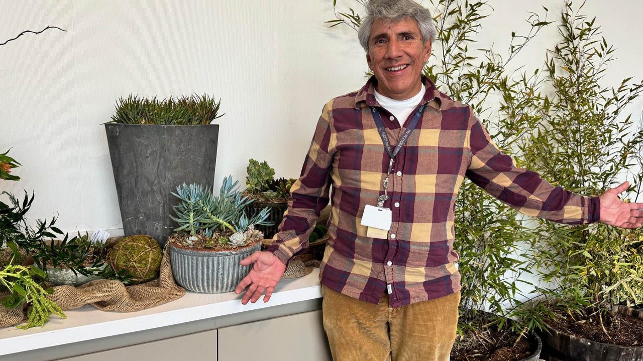The teacher is standing in front of a table of succulents while smiling.